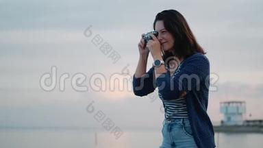 年轻女子在海边的老式相机上拍照。 一个有复古相机的女孩的肖像